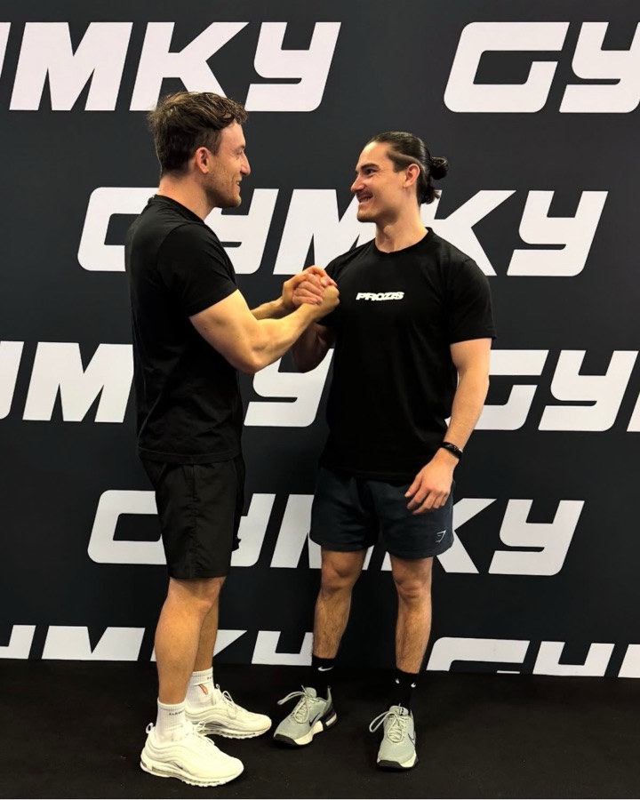 Zwei GYMKY Athleten begrüßen sich vor der GYMKY-Wand